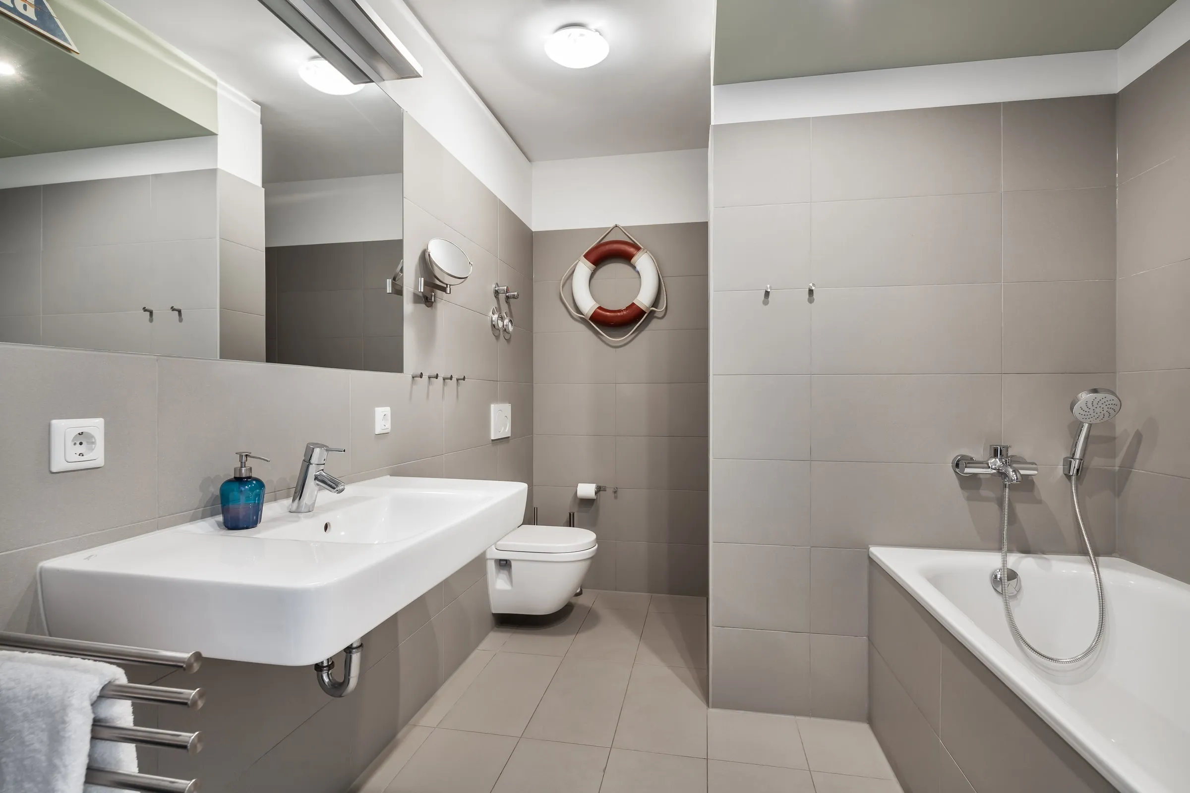 Das Bad mit Badewanne, Waschtisch und Rettungsring an der Wand