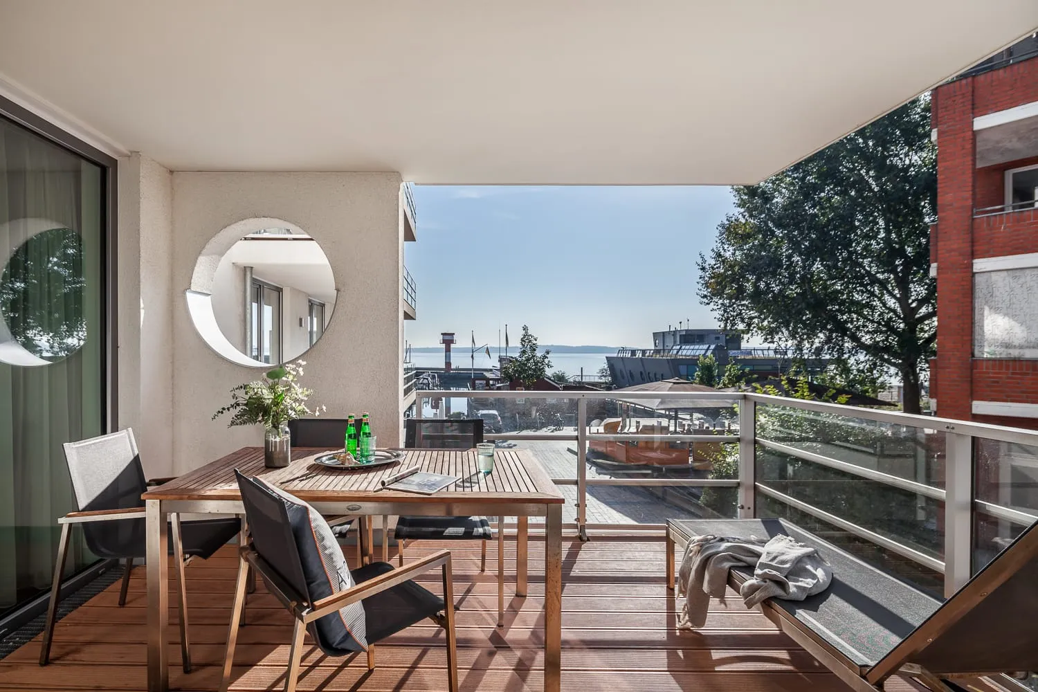 Die überdachte Loggia mit Tisch, Stühlen und Liegebank, Blick über den Hafen auf die Ostsee