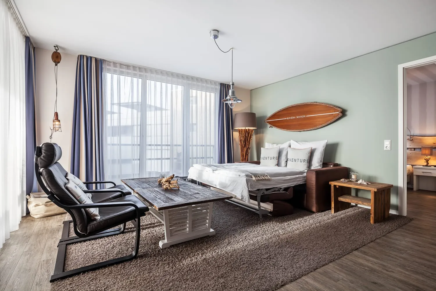 Der Wohnraum in der Breite: Sessel, Couchtisch und ausgezogenes Schlafsofa, links die bodentiefen Fenster